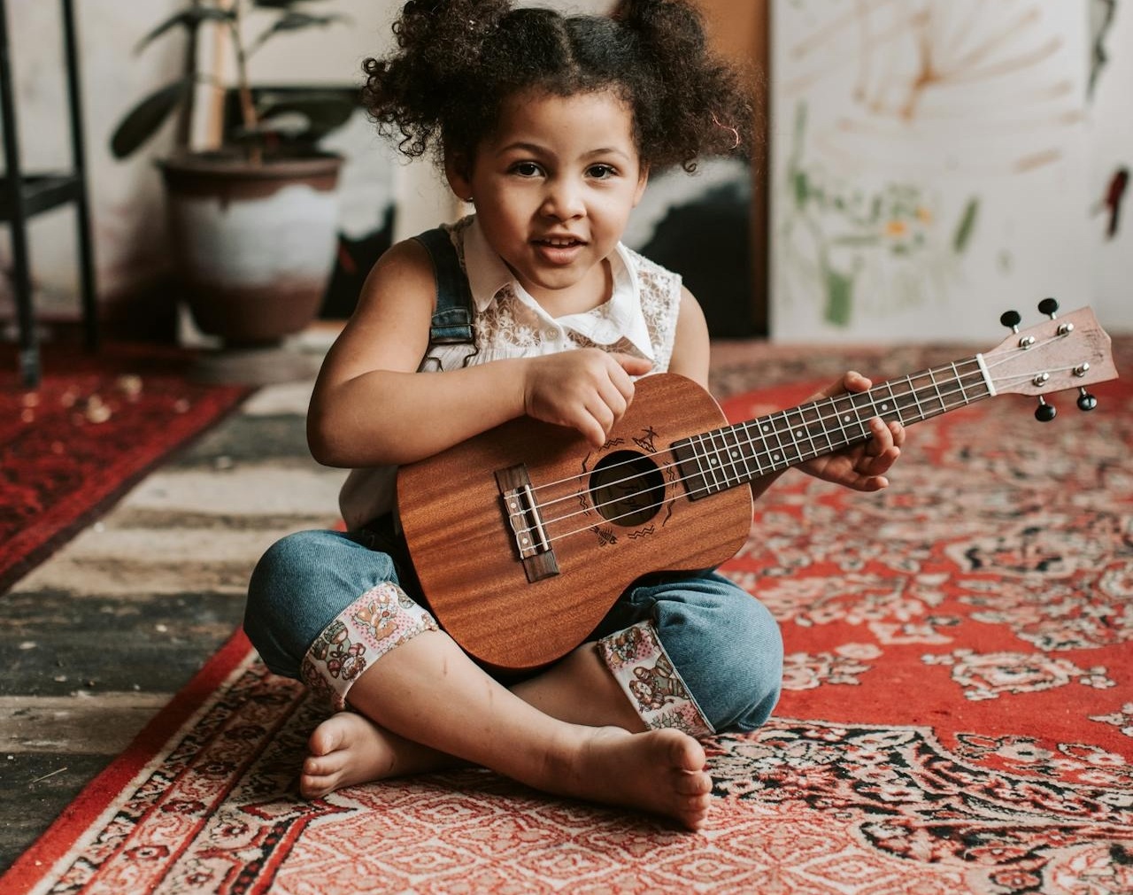 Dítě sedící na koberci v pokojíčku držící malou kytaru.